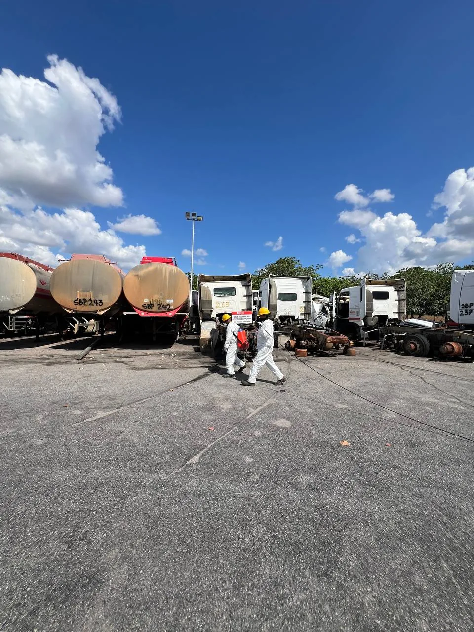 Dos operarios caminan con el equipo de aspersión entre cisternas y chutos estacionados.