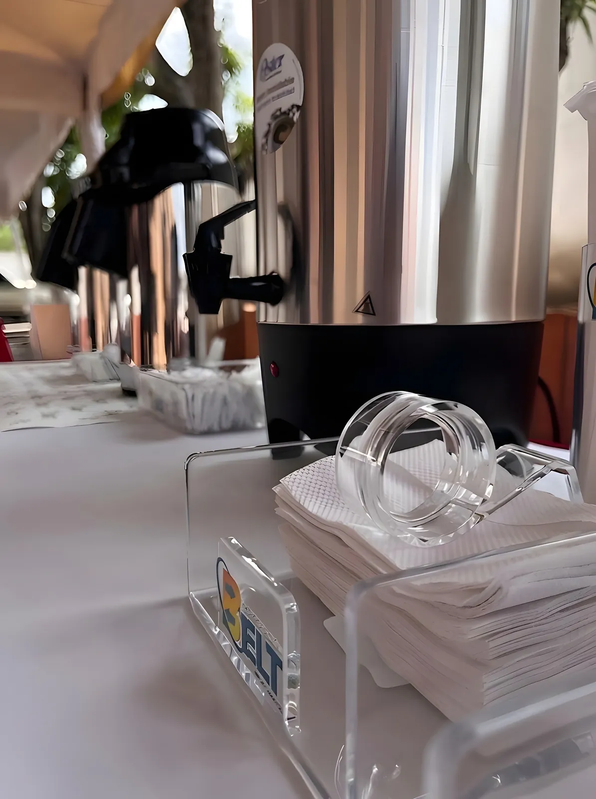 Termo de café de acero junto a un servilletero acrílico con el logo de BELT.