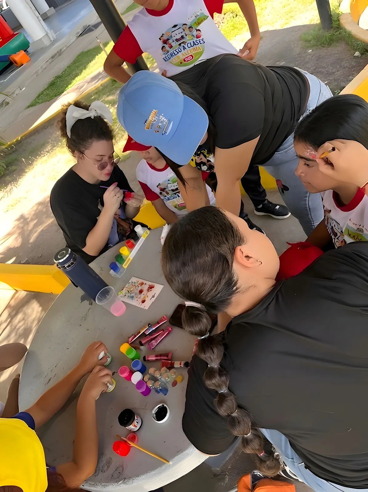 Integrantes del equipo pintan la cara de unas niñas en una mesa con témperas.