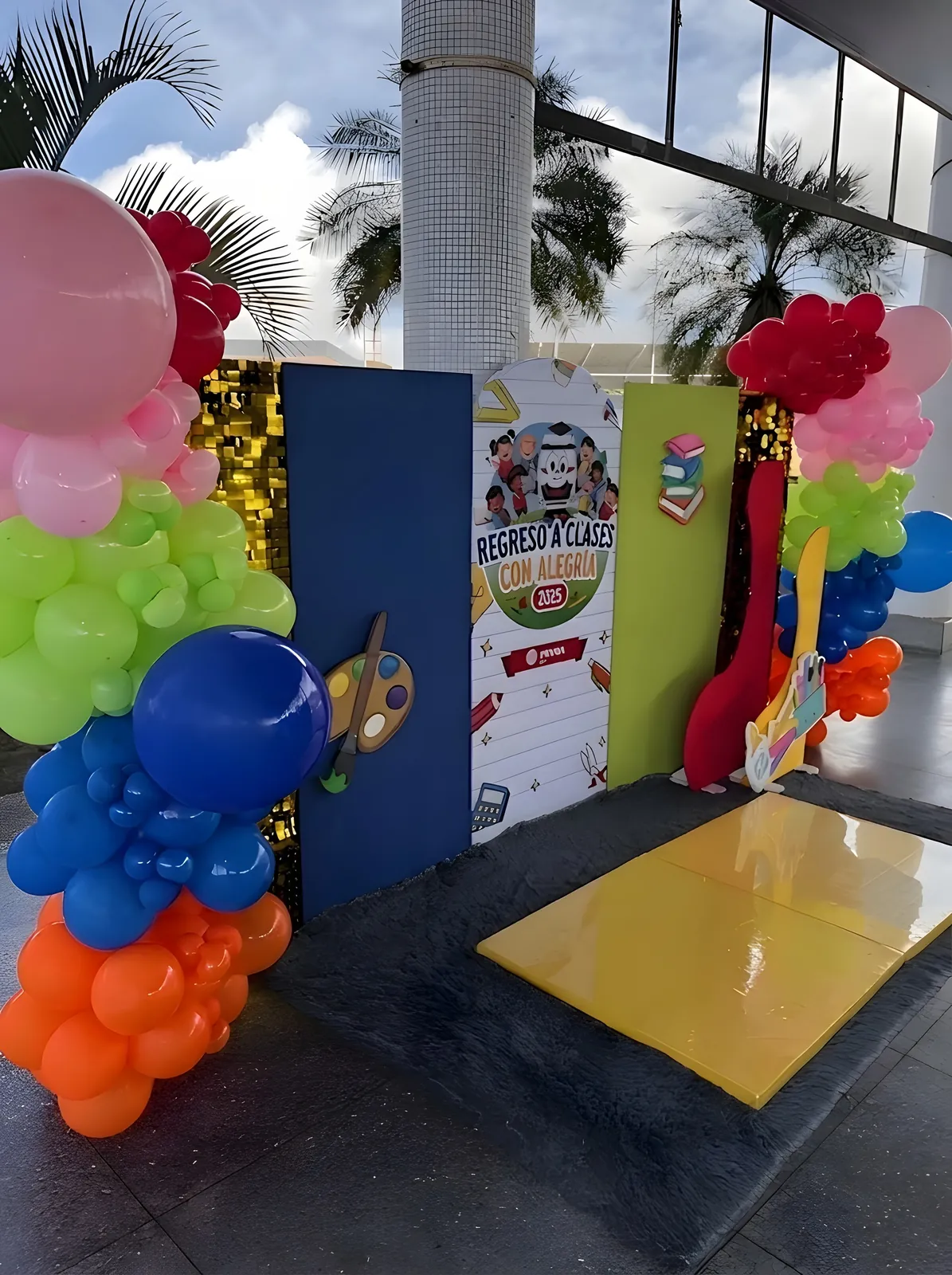 Photocall con columnas de globos de colores y el panel «Regreso a Clases con Alegría 2025».