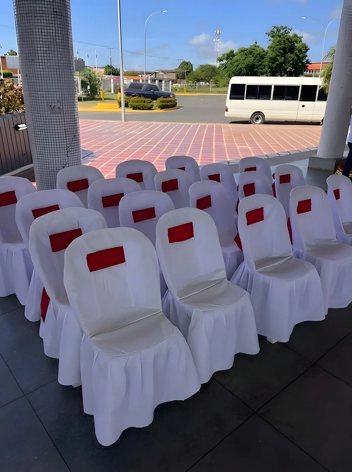Filas de sillas con forro blanco y banda roja bajo techo.